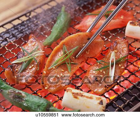 Stock Image - Slices of pork grilled over charcoal. Fotosearch