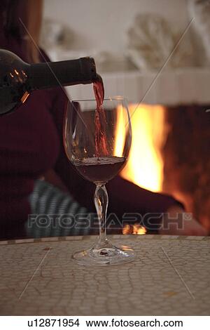 Picture - Woman pouring wine in glass, sitting at the fireplace. Fotosearch