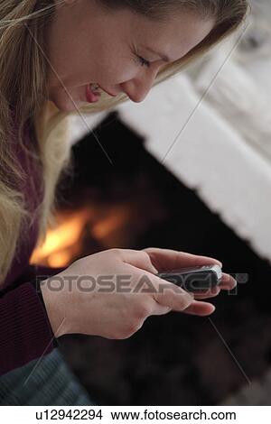 Woman using mobile phone by the fireplace, side view View Large Photo Image Picture - Woman using mobile phone by the fireplace, side view. Fotosearch