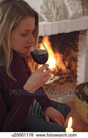 Young woman tasting glass of red wine by the fireplace, side view View Large Photo Image Stock Photo - Young woman tasting glass of red wine by the fireplace, side view. Fotosearch