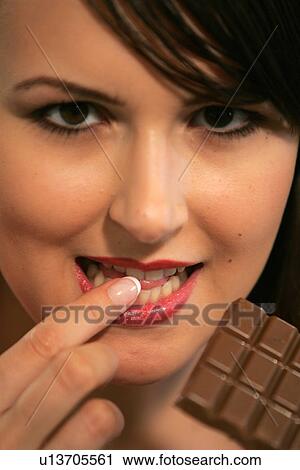 Stock Image - Young woman eating bar of chocolate, portrait, close up. Fotosearch