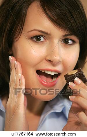 Picture - Young woman eating chocolate candy, portrait, close up. Fotosearch