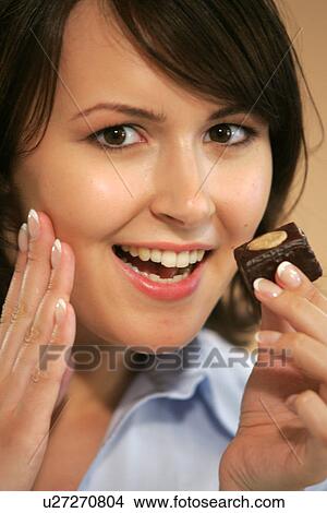 Picture - Young woman eating chocolate candy, portrait, close up. Fotosearch