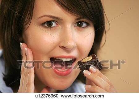 Stock Image - Young woman eating chocolate candy, portrait, close up. Fotosearch