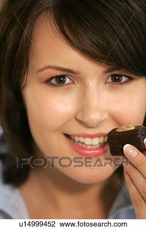 Stock Image - Young woman eating chocolate candy, portrait, close up. Fotosearch