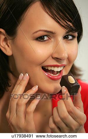 Stock Image - Young woman eating chocolate candy, portrait, close up. Fotosearch