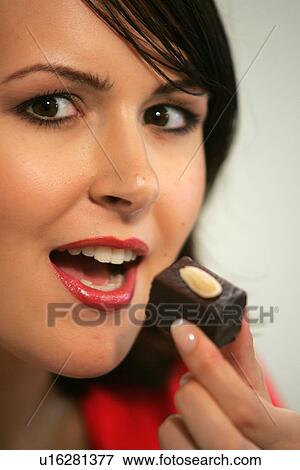 Stock Photo - Young woman eating chocolate candy, portrait, close up. Fotosearch