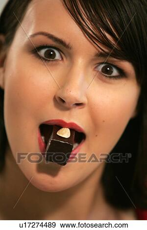 Stock Photo - Young woman eating chocolate candy, portrait, close up. Fotosearch