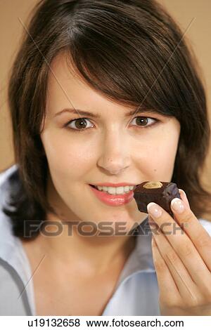 Stock Photo - Young woman eating chocolate candy, portrait, close up. Fotosearch