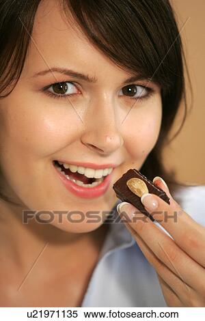 Stock Photography - Young woman eating chocolate candy, portrait, close up. Fotosearch