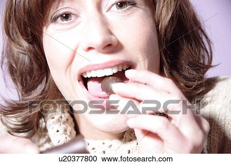 Stock Image - Woman eating piece of chocolate, portrait. Fotosearch