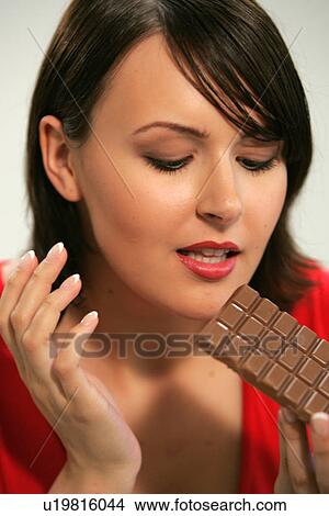 Picture - Young woman eating bar of chocolate, portrait, close up. Fotosearch