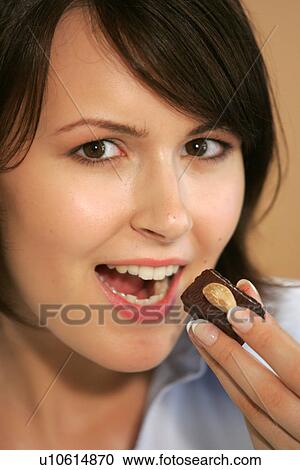 Stock Image - Young woman eating chocolate candy, portrait, close up. Fotosearch