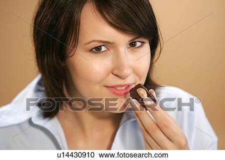 Stock Image - Young woman eating chocolate candy, portrait, close up. Fotosearch