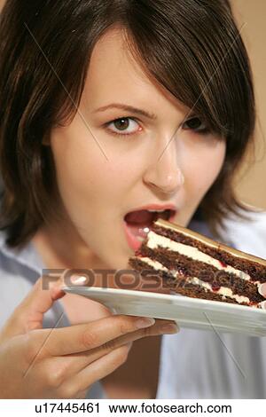 Stock Image - Young woman eating slice of chocolate cake, portrait, close up. Fotosearch