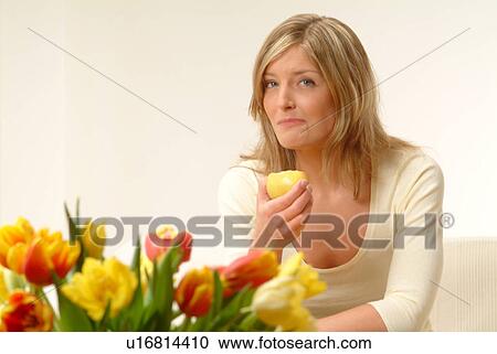 Stock Image - Woman eating apple, flowers in foreground. Fotosearch