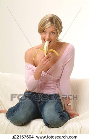 Picture - Woman eating banana on sofa. Fotosearch