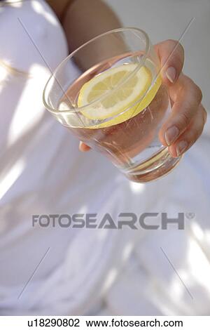 Woman holding glass of mineral water with slice of lemon in it, close up View Large Photo Image Stock Image - Woman holding glass of mineral water with slice of lemon in it, close up. Fotosearch