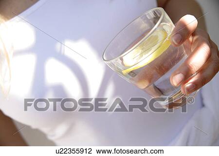Woman holding glass of mineral water with slice of lemon in it, close up View Large Photo Image Stock Image - Woman holding glass of mineral water with slice of lemon in it, close up. Fotosearch