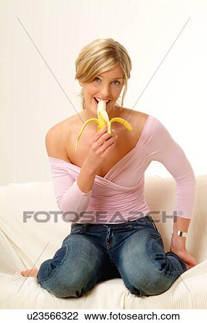 Stock Image - Woman on sofa eating banana. Fotosearch