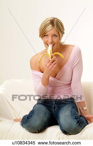 Stock Photography - Woman on sofa eating banana. Fotosearch
