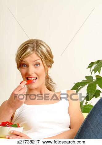Stock Photo - Woman on sofa eating red pepper. Fotosearch