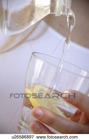 Stock Photo - Woman pouring mineral water in glass with slice of lemon in it, close up. Fotosearch