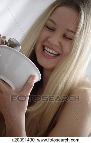 Stock Image - Young blond woman eating bowl of cereals, laughing, close up. Fotosearch