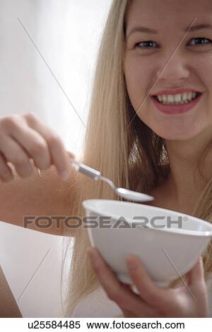 Stock Photography - Young blond woman eating bowl of cereals, laughing, close up. Fotosearch