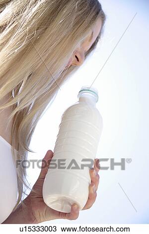 Stock Image - Young blond woman holding milk bottle, view from below. Fotosearch