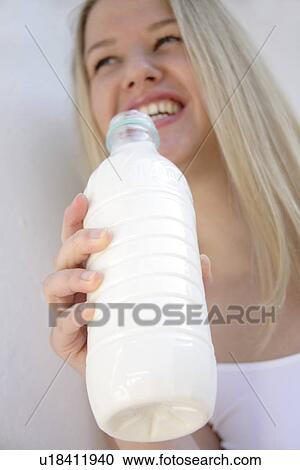 Stock Image - Young blond woman holding milk bottle, view from below. Fotosearch