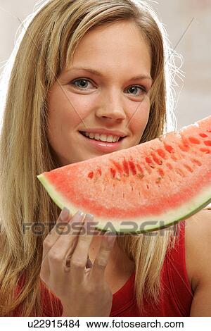 Picture - Young woman with long blond hair eating a slice of watermelon, portrait. Fotosearch