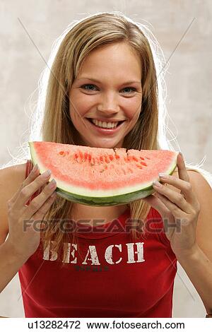 Stock Image - Young woman with long blond hair eating a slice of watermelon, portrait. Fotosearch
