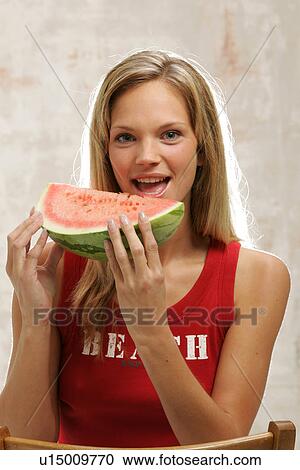 Stock Image - Young woman with long blond hair eating a slice of watermelon, portrait. Fotosearch