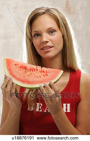 Stock Image - Young woman with long blond hair eating a slice of watermelon, portrait. Fotosearch