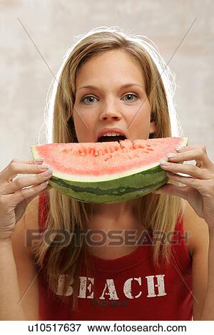 Stock Photo - Young woman with long blond hair eating a slice of watermelon, portrait. Fotosearch