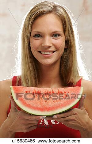 Stock Photograph - Young woman with long blond hair eating a slice of watermelon, portrait. Fotosearch