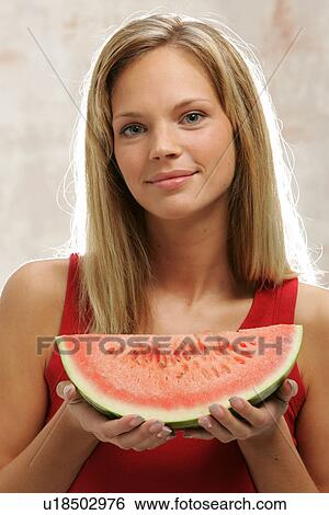 Stock Photograph - Young woman with long blond hair eating a slice of watermelon, portrait. Fotosearch
