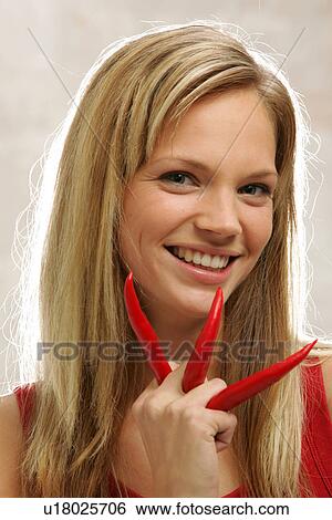 Stock Photograph - Young woman with long blond hair holding three chili peppers, portrait. Fotosearch