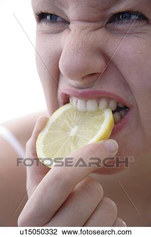 Stock Image - Young blond woman biting in slice of lemon, close up. Fotosearch