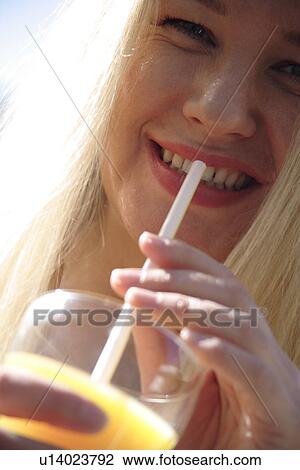 Young blond woman drinking orange juice with straw, close up View Large Photo Image Stock Image - Young blond woman drinking orange juice with straw, close up. Fotosearch