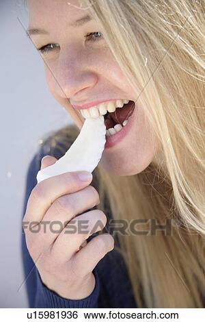 Stock Photograph - Young blond woman eating a piece of coconut, close up. Fotosearch