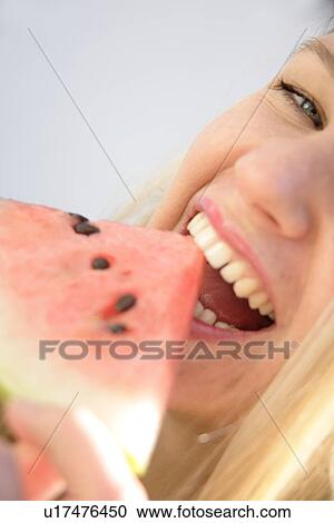 Stock Image - Young blond woman eating a slice of watermelon, close up. Fotosearch