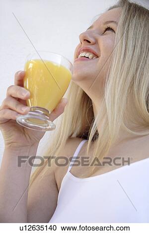 Stock Image - Young blond woman holding glass of orange juice, view from below. Fotosearch