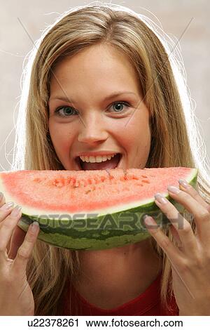 Stock Image - Young woman with long blond hair eating a slice of watermelon, portrait. Fotosearch
