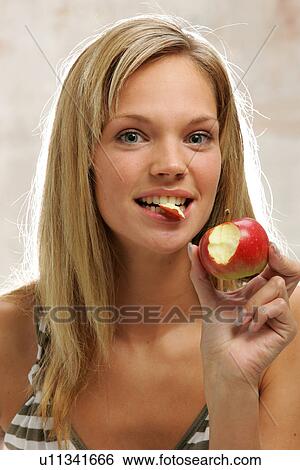 Stock Photograph - Young woman with long blond hair eating an apple, portrait. Fotosearch