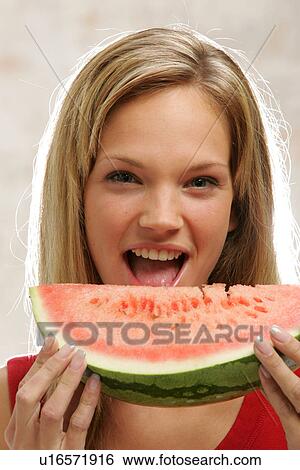 Stock Photograph - Young woman with long blond hair eating a slice of watermelon, portrait. Fotosearch