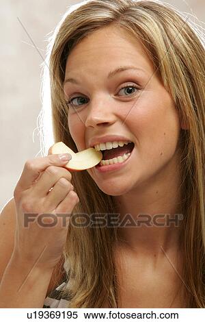 Stock Photography - Young woman with long blond hair eating an apple, portrait. Fotosearch