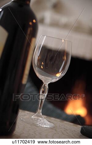 Stock Photo - Bottle and glass of wine on a table in front of the fireplace, stillife. Fotosearch