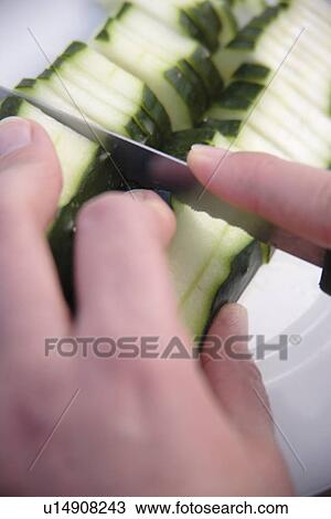 Stock Image - Peeling and slicing fresh cucmber for salad, close up. Fotosearch